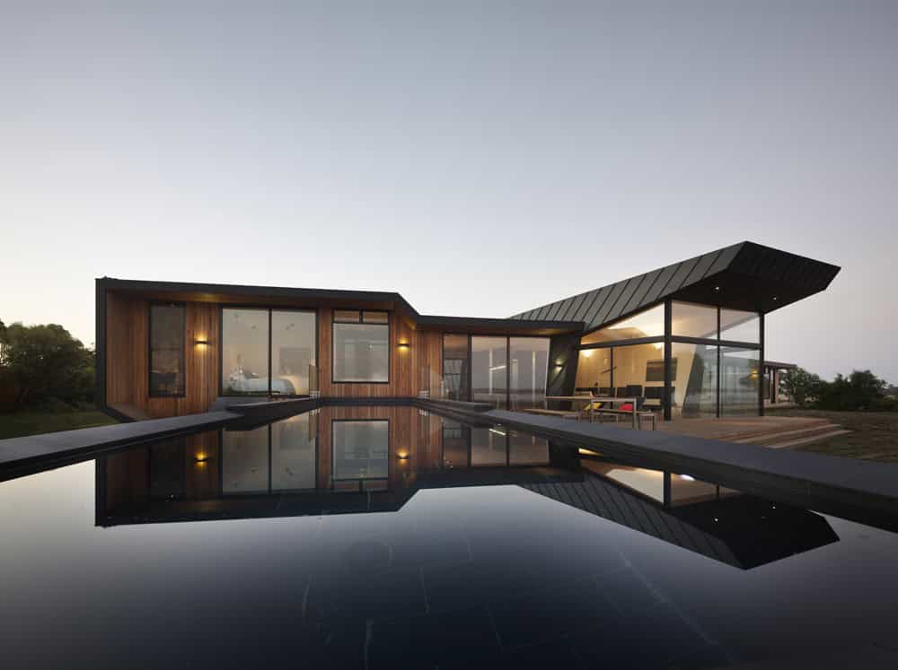 Modern luxury house with wooden and glass architecture reflected in a pool at sunset, showcasing innovative design and contemporary home architecture.