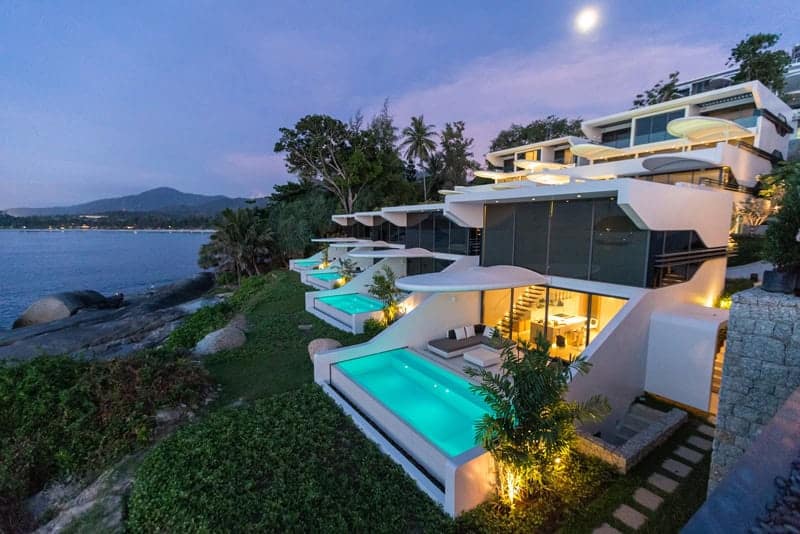 Modern luxury beachfront villa with infinity pools and sleek architectural design overlooking the ocean, featuring innovative curves and expansive glass windows.