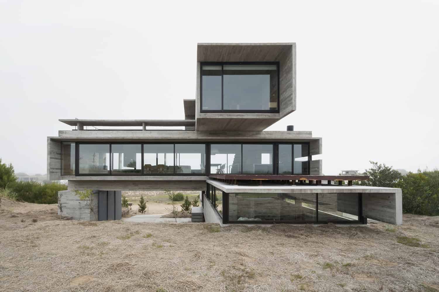 Sleek modern house with concrete and glass architecture, featuring a unique cantilevered design and expansive windows, set in a natural landscape.