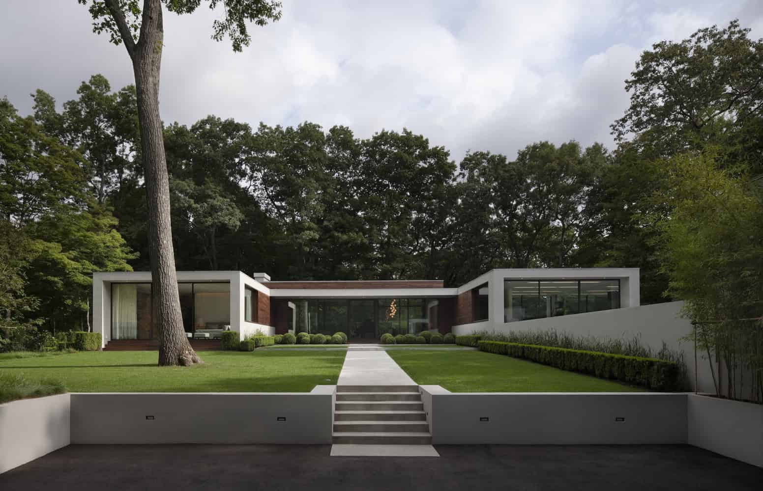Modern minimalist house with large glass windows, clean lines, and lush green landscaping. Architectural design emphasizing sleek contemporary style and integration with nature.