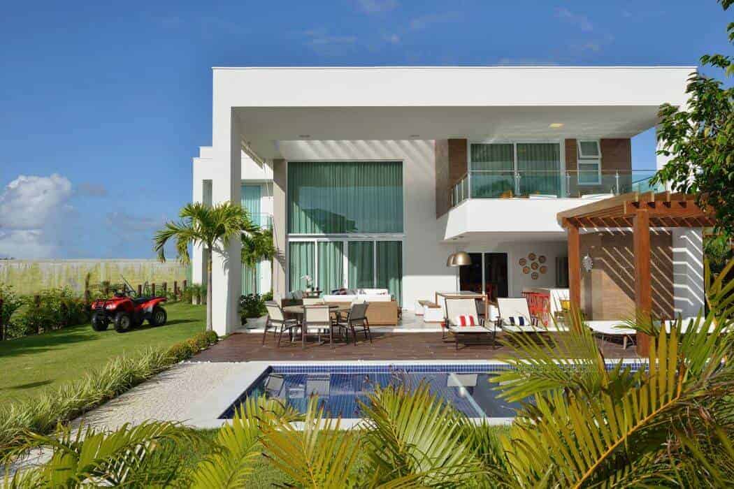 Modern luxury house exterior with outdoor pool, patio furniture, and tropical landscaping under a clear blue sky.
