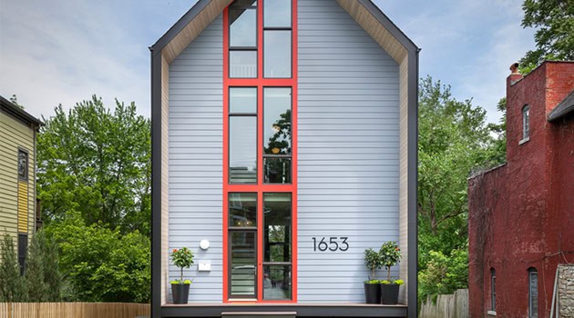 Modern minimalist house with gray siding, red accents, and large vertical windows.