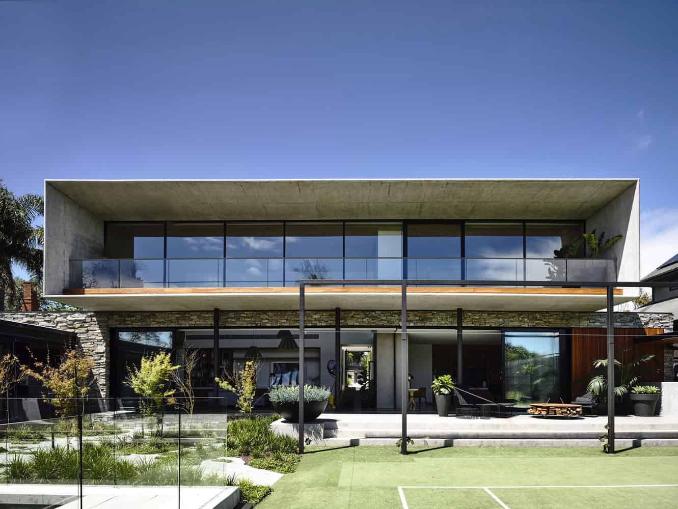 Contemporary modern house with minimalist concrete and glass design, featuring large windows, outdoor patio, green landscaping, and sleek architectural elements.