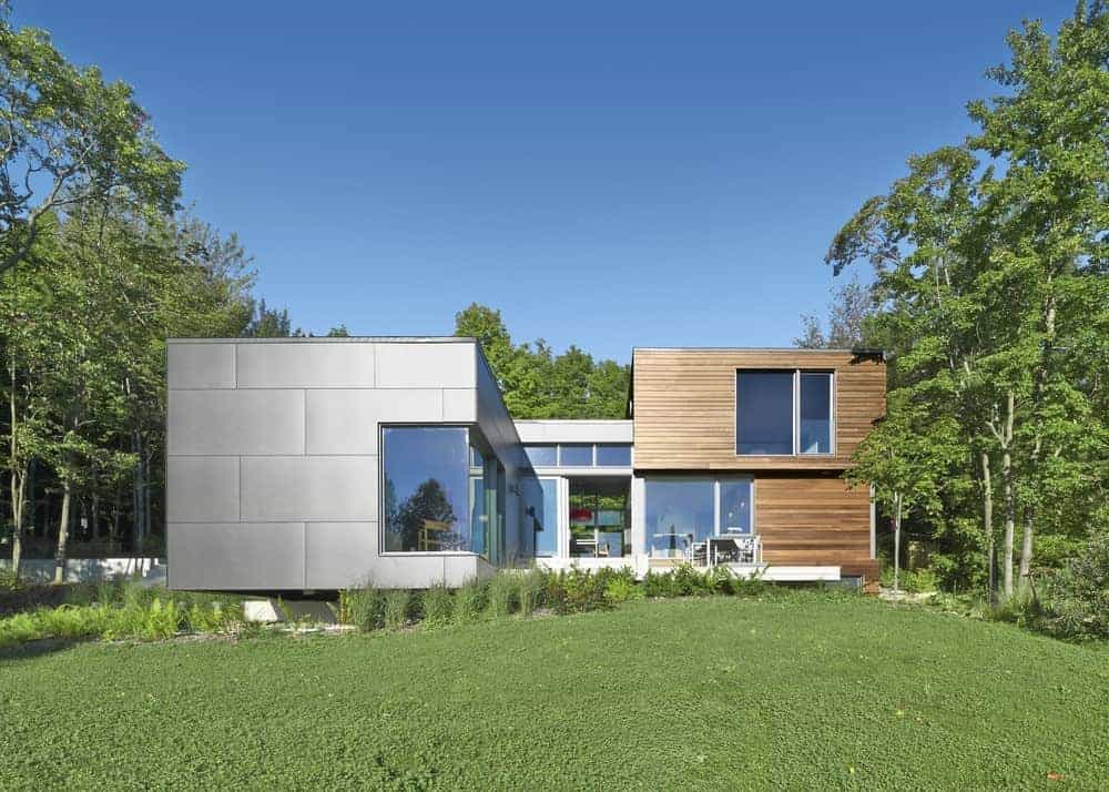 Contemporary modern house with sleek metal and wood exterior, large windows, and surrounding lush greenery, showcasing innovative architecture and stylish design.