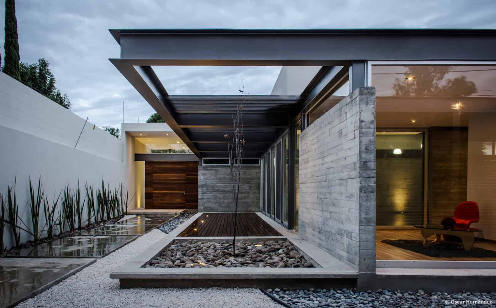 Contemporary modern house exterior with minimalist design, concrete walls, glass sliding doors, and landscaped garden featuring water accents and decorative stones.