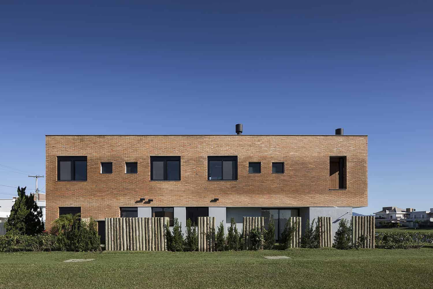 Contemporary minimalist brick residential building with modern windows, clean lines, and a landscaped garden under a clear blue sky.