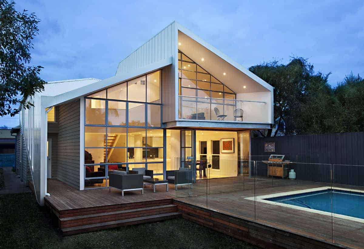 Modern contemporary house with large glass windows, outdoor wooden deck, and swimming pool, showcasing innovative architectural design and stylish interior lighting.