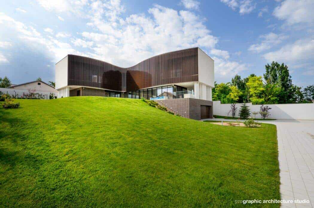 Futuristic modern house with curvy roof design and large glass windows on a lush green hillside.