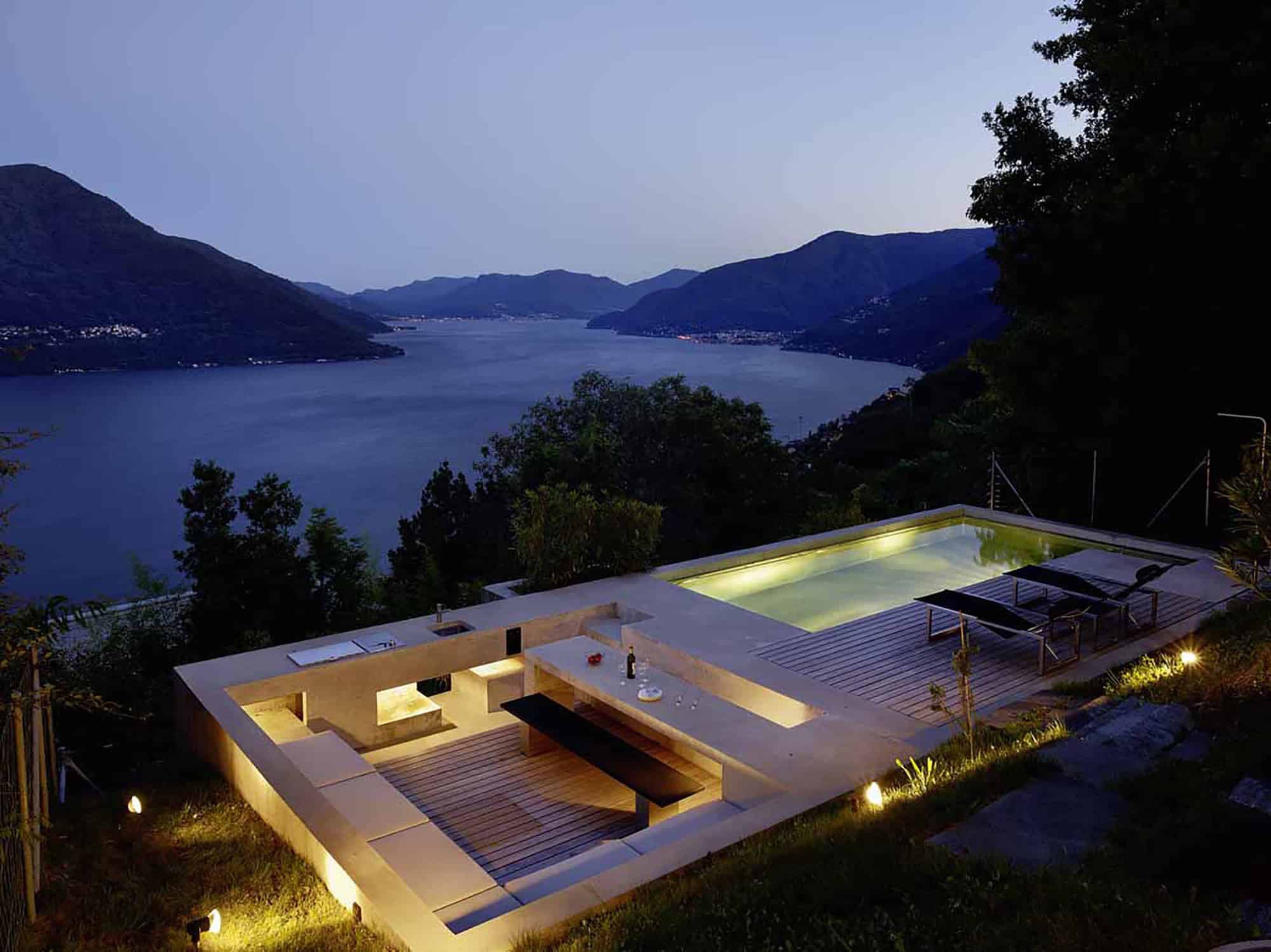Breathtaking infinity pool overlooking a serene lake and mountain landscape at dusk, featuring modern design with lounge chairs and ambient lighting, perfect for luxury outdoor living.