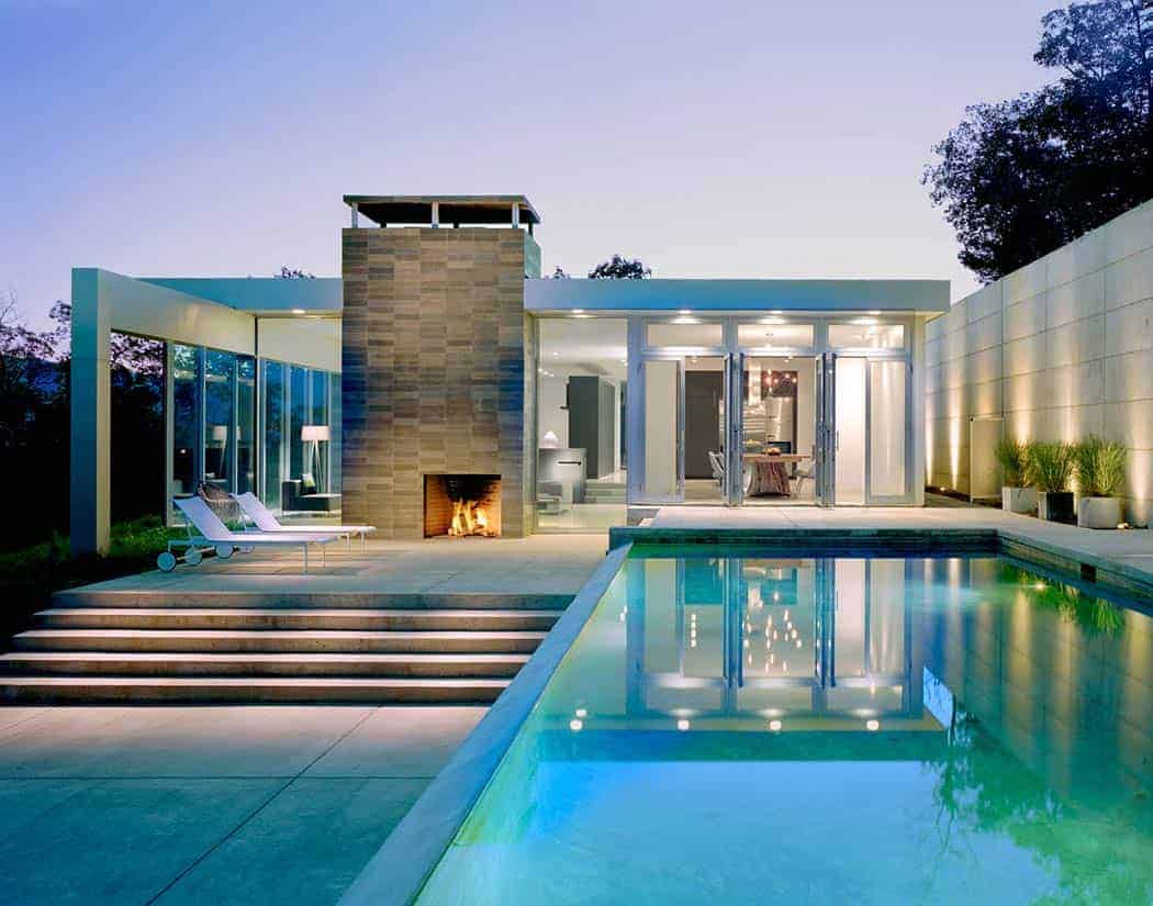 Modern minimalist house with glass walls and outdoor fireplace, featuring a sleek swimming pool, stylish lounge chairs, and contemporary landscaping. Elegant architecture and open living space design.
