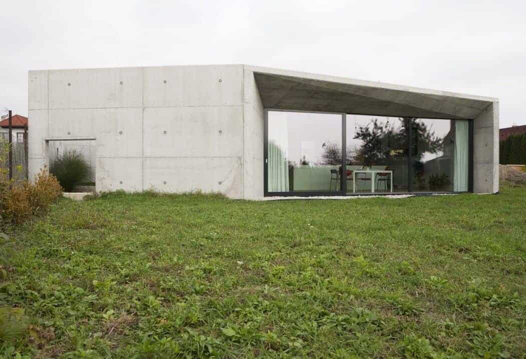 Contemporary minimalist concrete house with large glass windows, modern architecture, and sleek design on a lush green lawn, showcasing innovative residential architectural styles.
