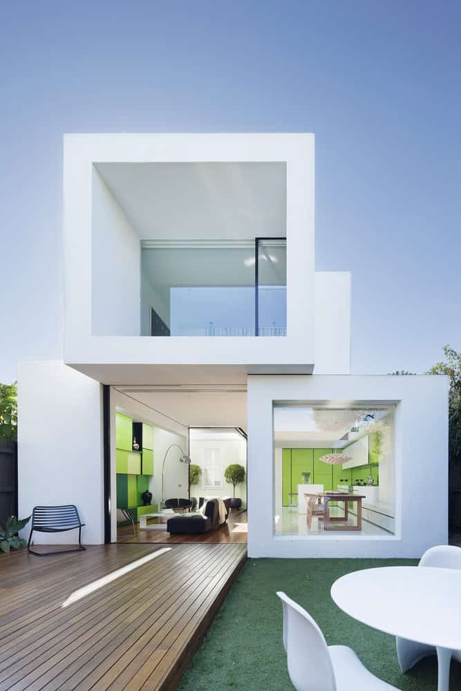 Modern minimalist white contemporary house with large glass windows and green interior accents, featuring sleek architecture, outdoor deck, and vibrant garden space.