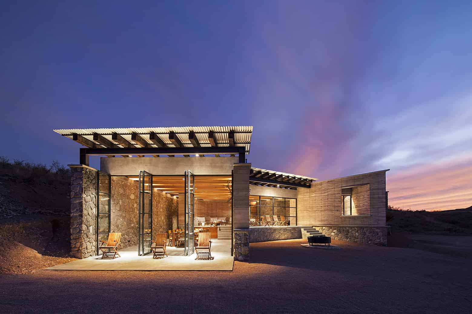 Contemporary modern house with a unique architectural design featuring stone and wood elements, large glass doors, and a stunning sunset background.