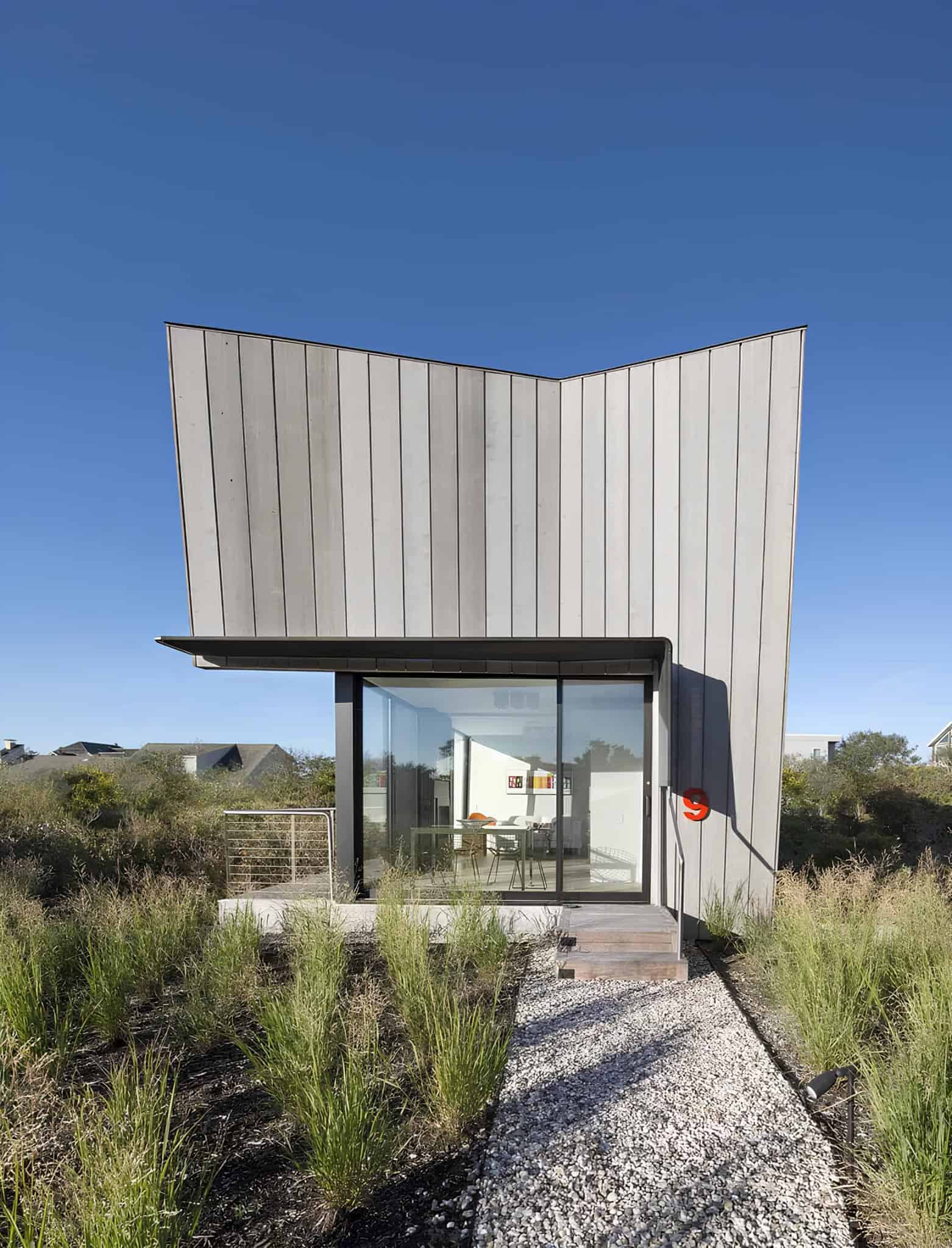 Contemporary modern house with innovative architecture, featuring sleek siding, large glass windows, and designed for a natural landscape setting. The structure embodies minimalism and modern aesthetic appeal.