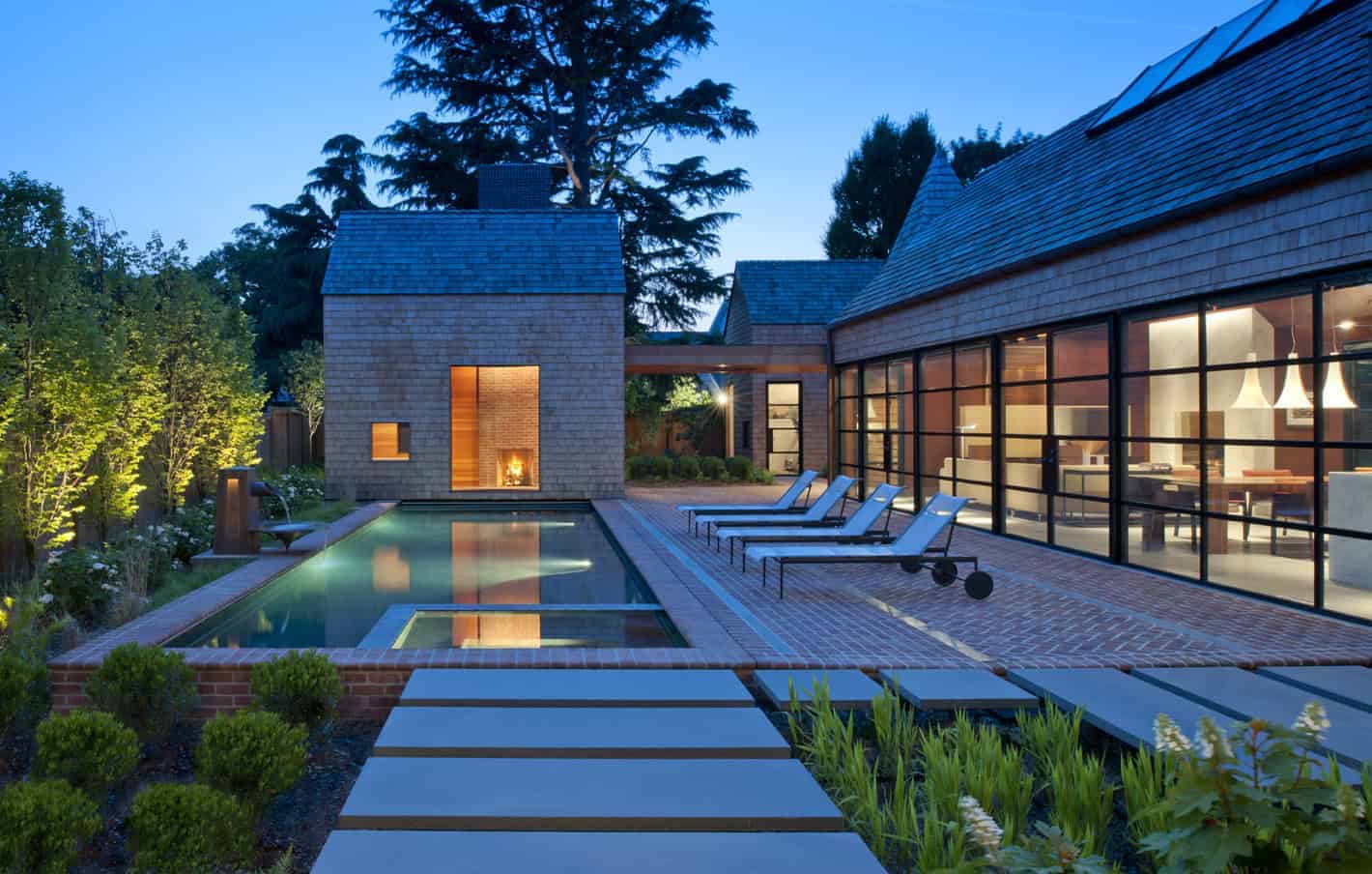 Modern luxury house with outdoor swimming pool, contemporary architecture, spacious patio, and large glass windows with interior lighting, harmonizing with lush garden surroundings.