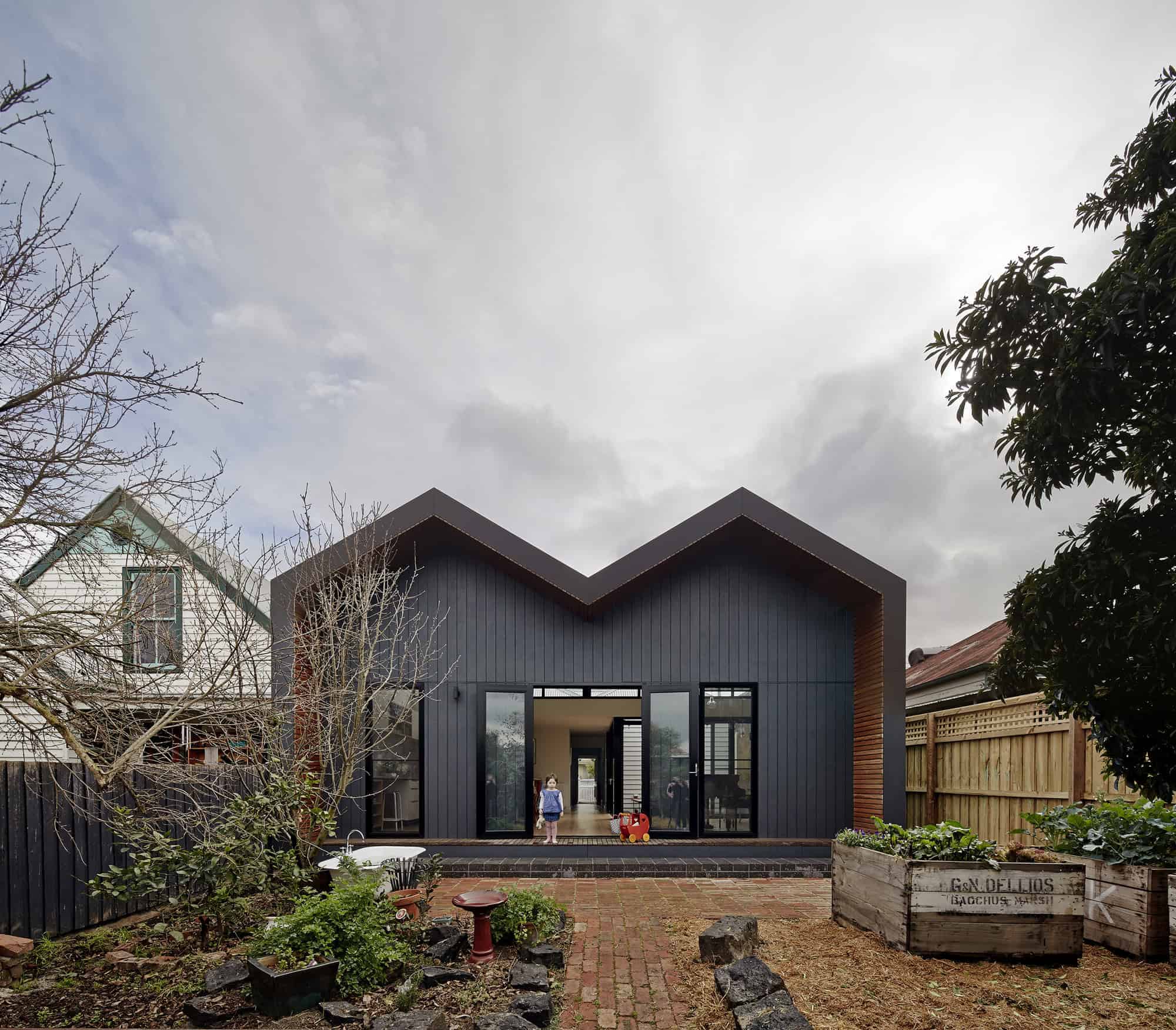 Modern black metal house with unique angular roof design, large glass doors, and contemporary architecture in a landscaped backyard setting.