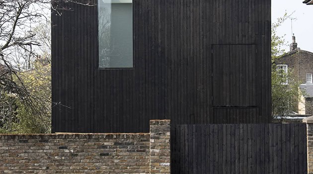 Modern minimalist black wooden house exterior with vertical siding and a brick boundary wall, showcasing contemporary urban architectural design.