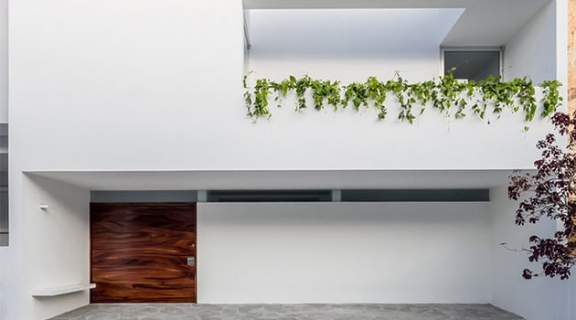 Sleek modern house facade with minimalist white exterior, wooden garage door, and green balcony plants emphasizing contemporary architecture and innovative design.