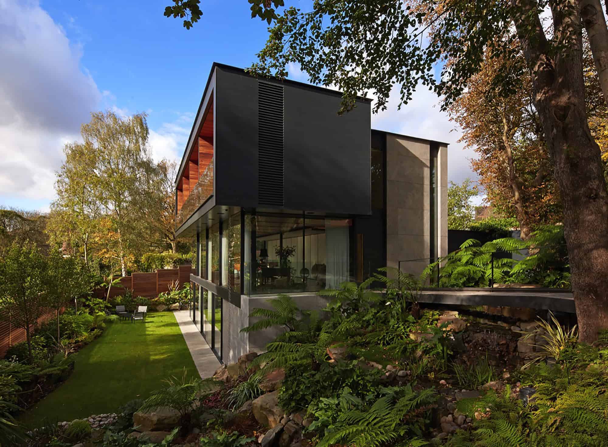 Sleek modern house with large glass windows, surrounded by lush greenery and trees, showcasing contemporary architecture and landscape design.