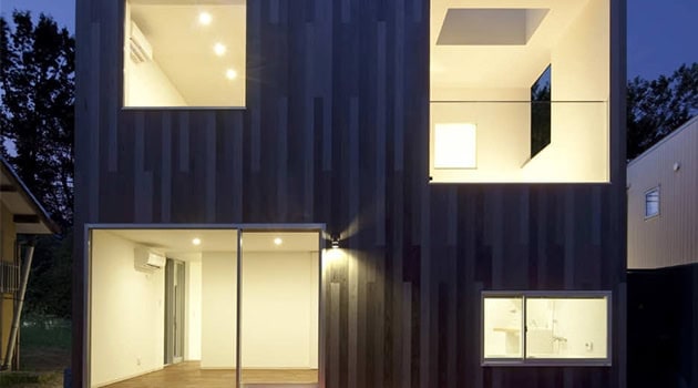 Modern black cladding house with large glass windows and interior lighting, showcasing contemporary architecture design and innovative building materials.