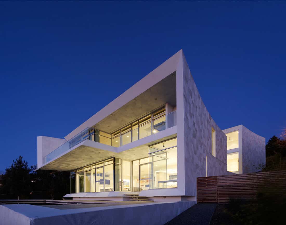 Modern minimalist architecture house with large glass windows and clean geometric design at twilight.