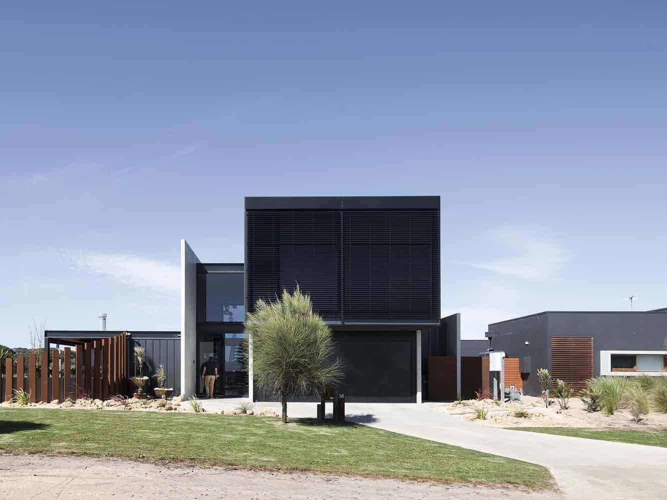 Modern black and gray minimalist residential house with clean lines, contemporary architecture, and outdoor landscape design featuring desert plants and a well-maintained lawn.