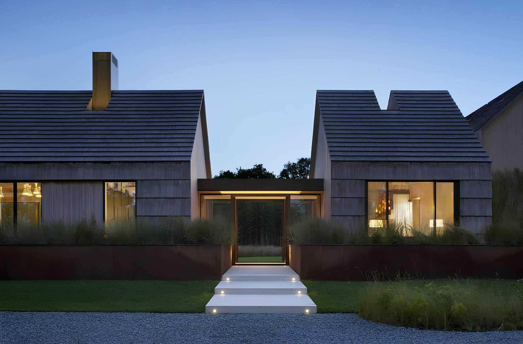 Contemporary modern house with sleek wooden exterior and large glass windows showcasing stylish interior lighting at dusk.