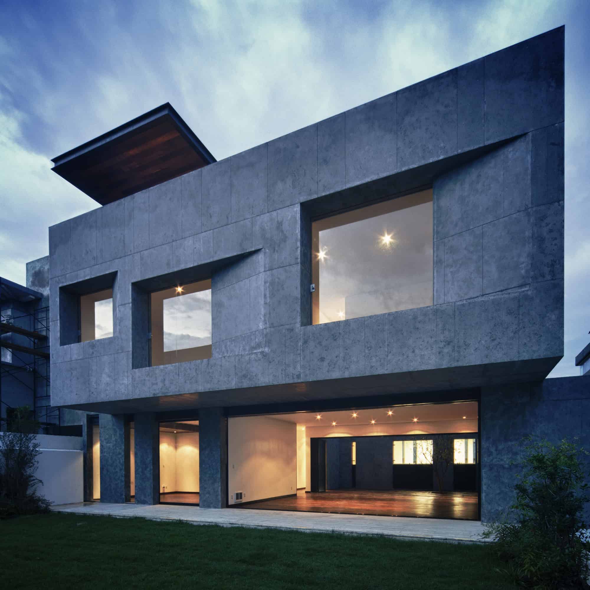 Sleek modern concrete house with large windows and contemporary architectural design, illuminated at dusk.