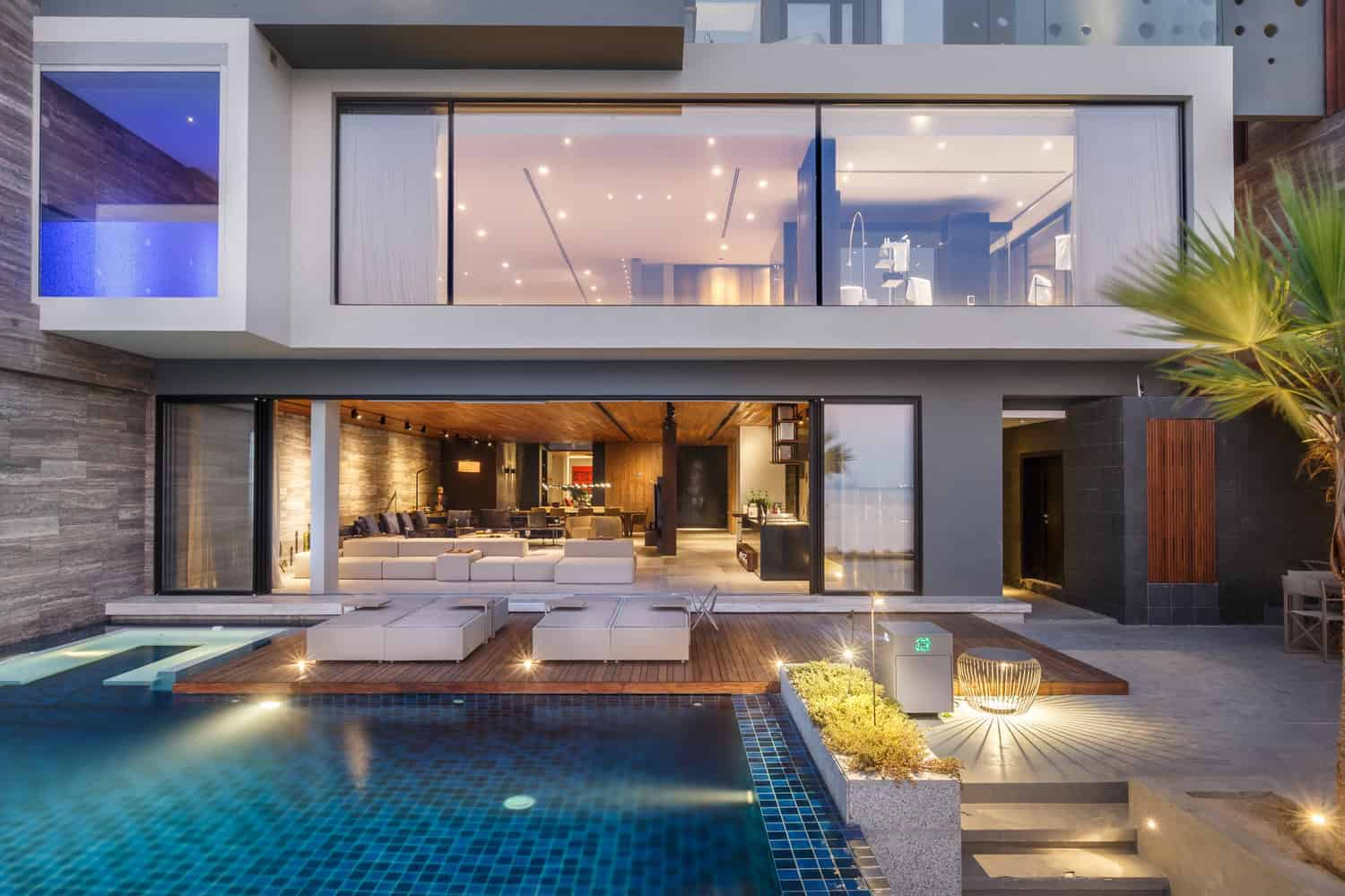 Luxurious modern house with a swimming pool, spacious outdoor lounge, and large glass windows showcasing contemporary architectural design and stylish interior decor.