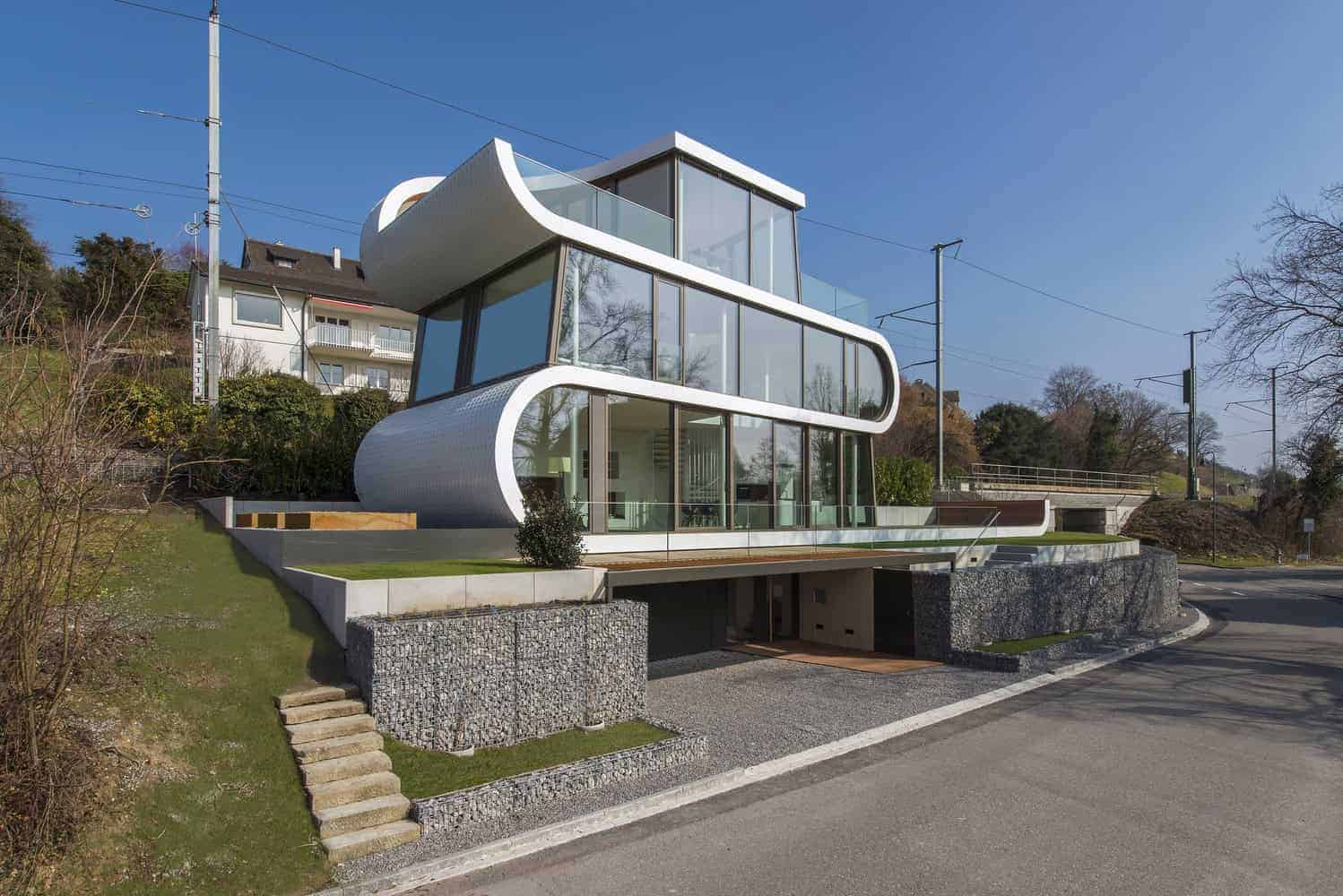 Futuristic modern house with curved white exterior, large glass windows, and innovative architecture design on a hillside.