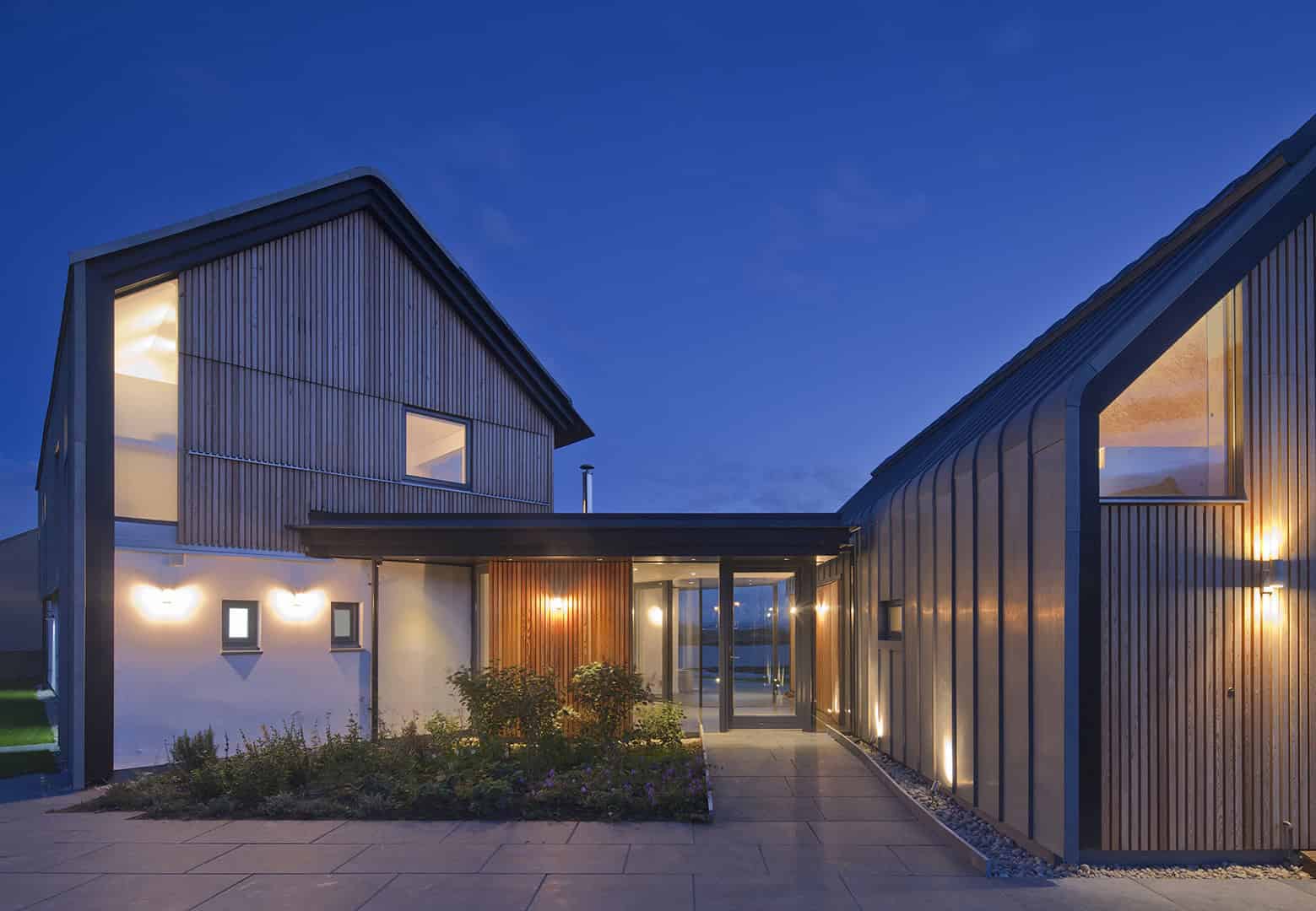 Contemporary modern house design with sharp geometric lines, wooden accents, and large glass windows, set against a twilight sky, showcasing innovative architecture and stylish exterior illumination.