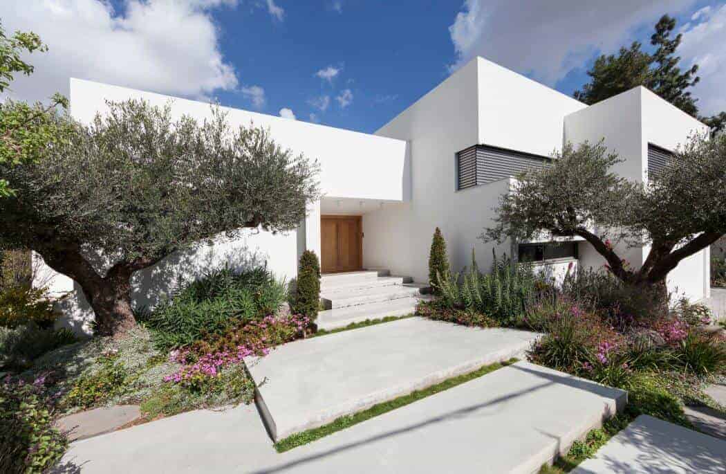 Contemporary white modern house with minimalist architecture, landscaped garden with trees and flowers, clean lines, and a bright blue sky, showcasing stylish residential design.