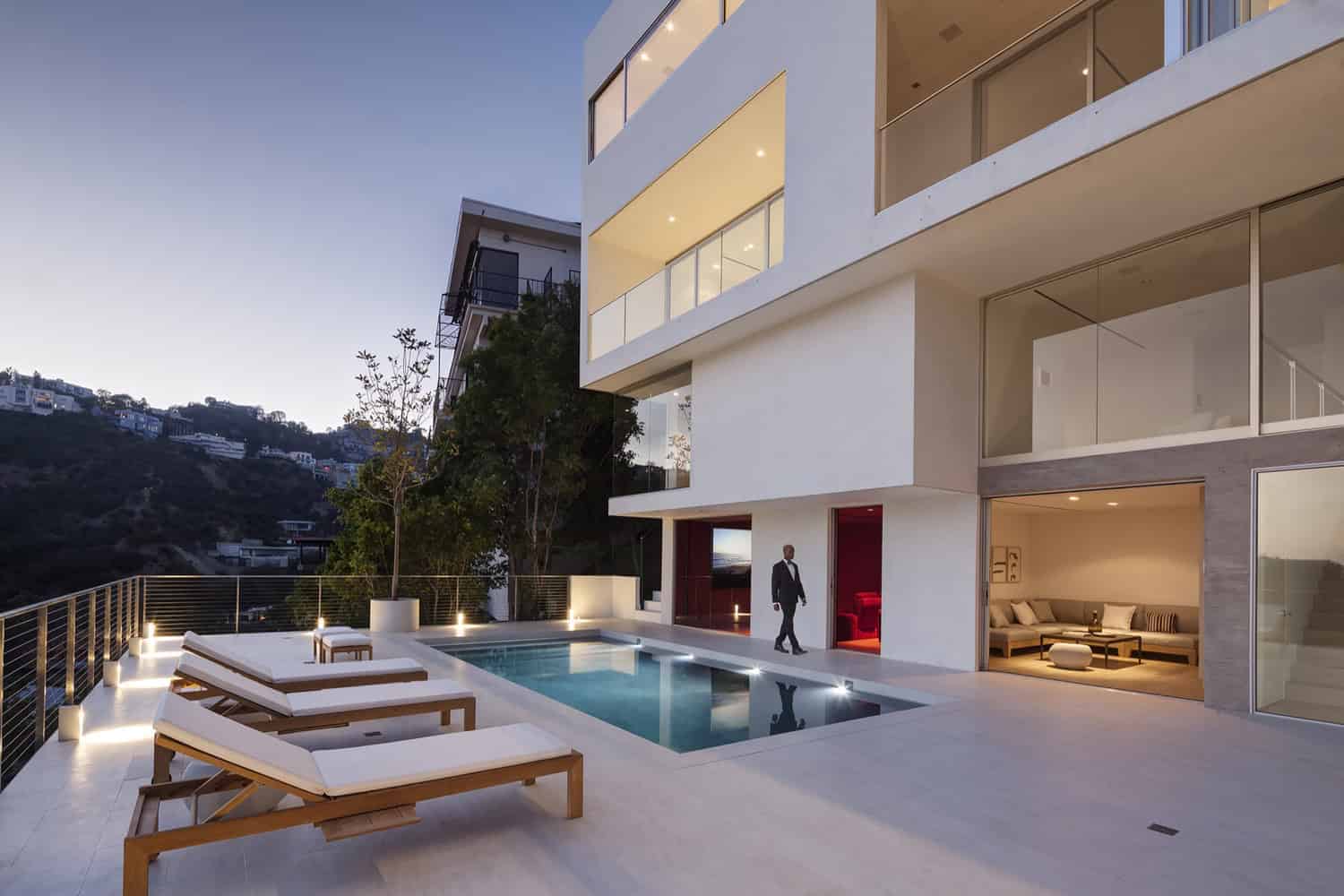 Contemporary modern house with an outdoor swimming pool, minimalist architecture, and panoramic city views at dusk. Elegant outdoor lounge area with sunbeds, outdoor lighting, and sleek design.