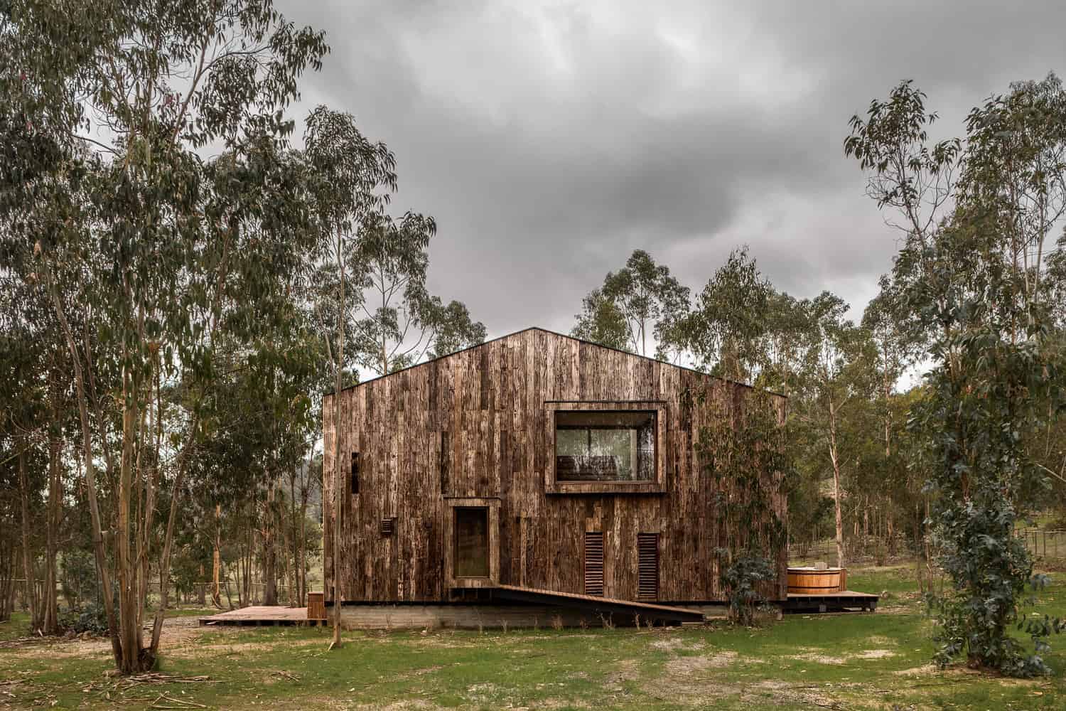 Sustainable modern wooden house surrounded by trees in a natural setting with cloudy sky, showcasing innovative architecture and eco-friendly design elements.