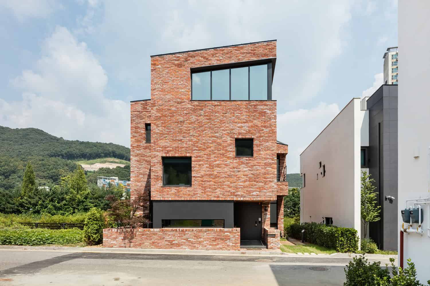 Contemporary modern brick house with geometric design, large windows, and minimalist exterior, situated in a scenic landscape, showcasing innovative architecture and urban housing design.