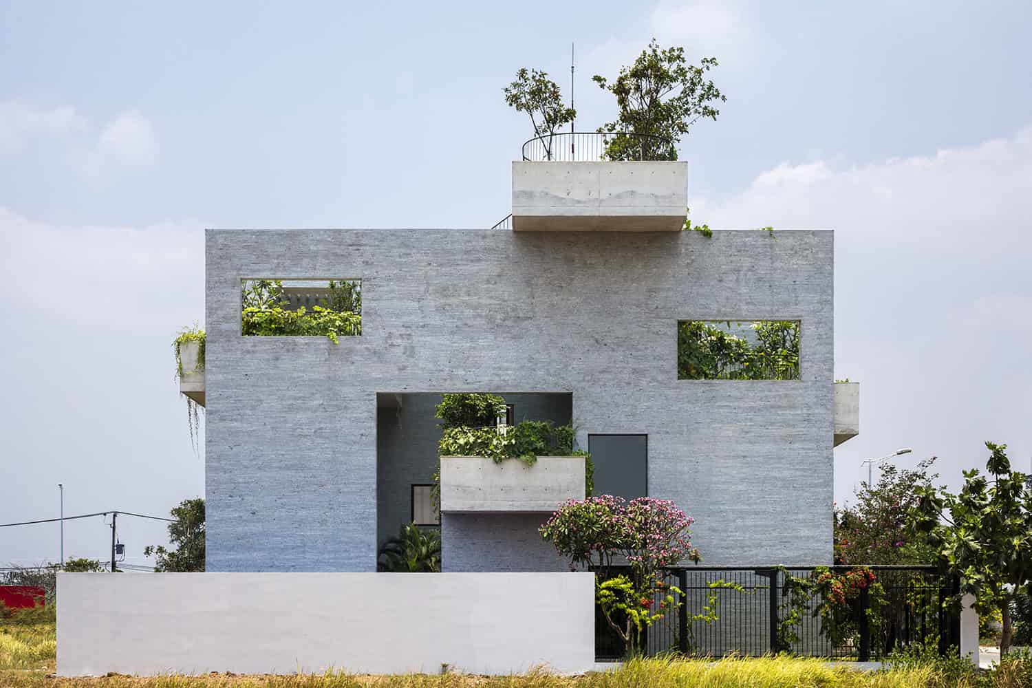 Contemporary minimalist residential building with geometric design, concrete walls, and rooftop garden, showcasing modern architecture and green living elements.