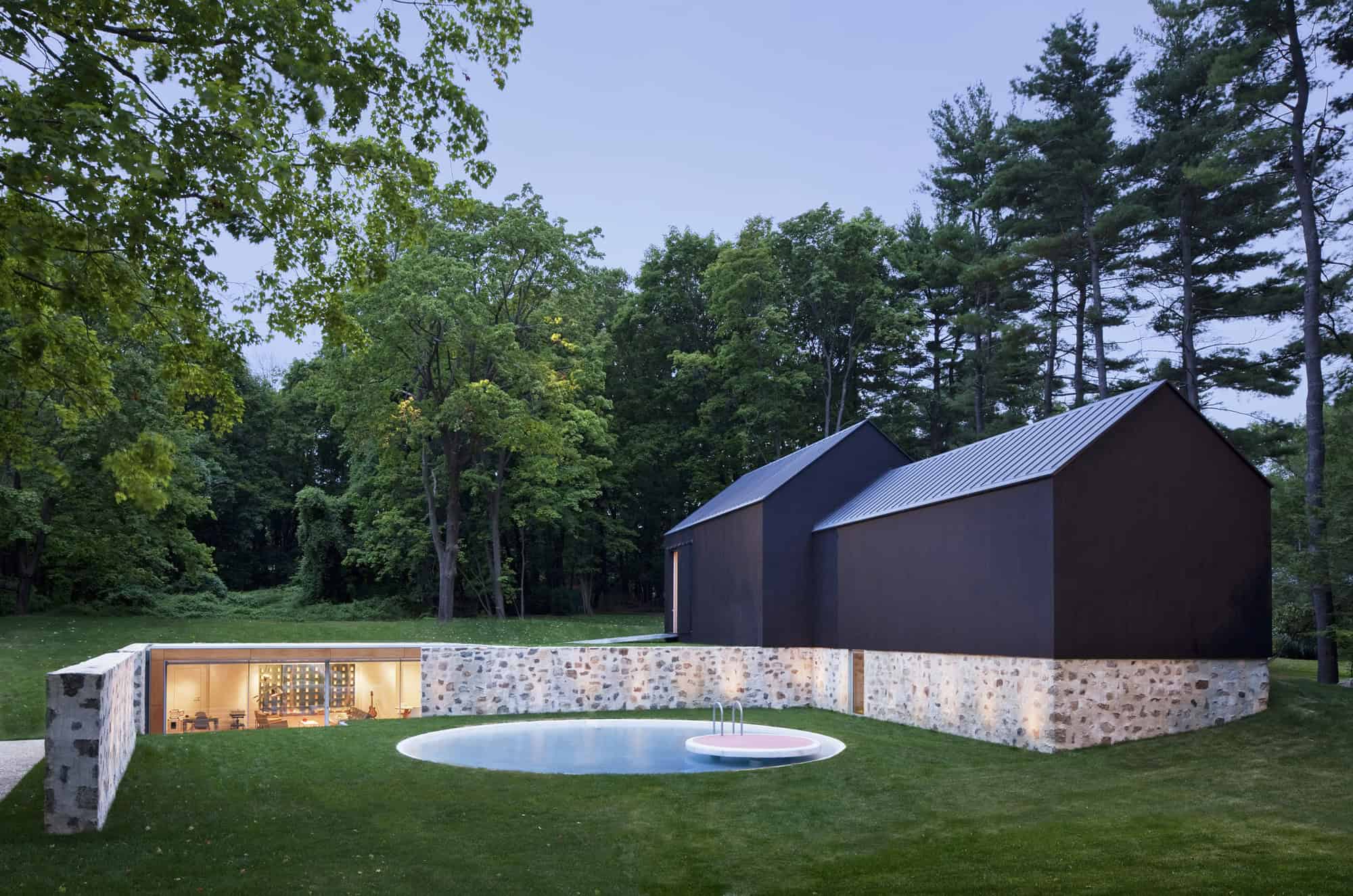 Modern black and stone house with swimming pool nestled in lush green forest, showcasing contemporary architecture and outdoor living design.