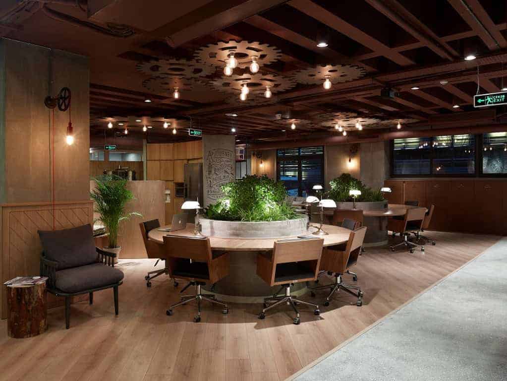 Modern office interior with wooden accents, cozy seating, and a central round table with green indoor plants, highlighting contemporary workspace design and eco-friendly decor.