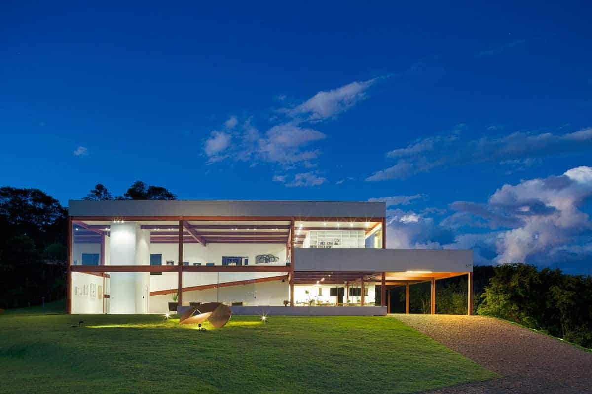 Futuristic modern house with large glass windows and minimalist design on lush green landscape under a vibrant evening sky.