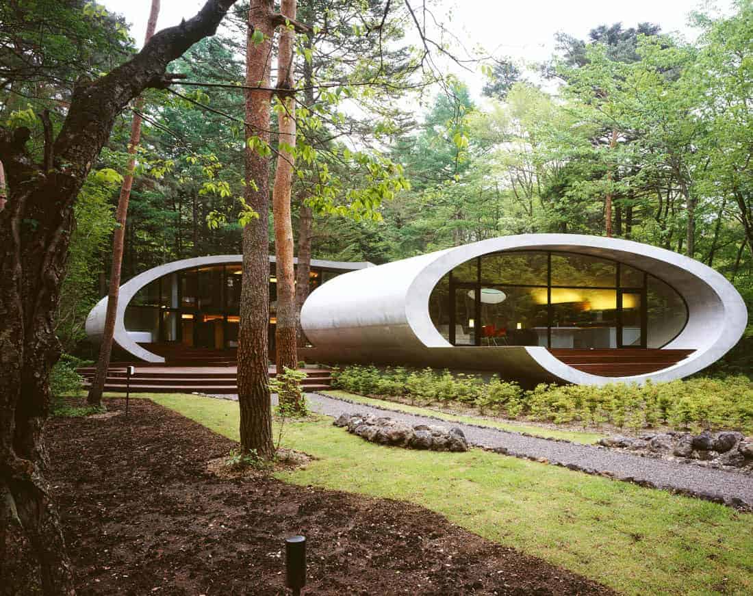 Futuristic modern house with sleek oval-shaped architecture surrounded by lush green forest, showcasing innovative design and eco-friendly architecture.