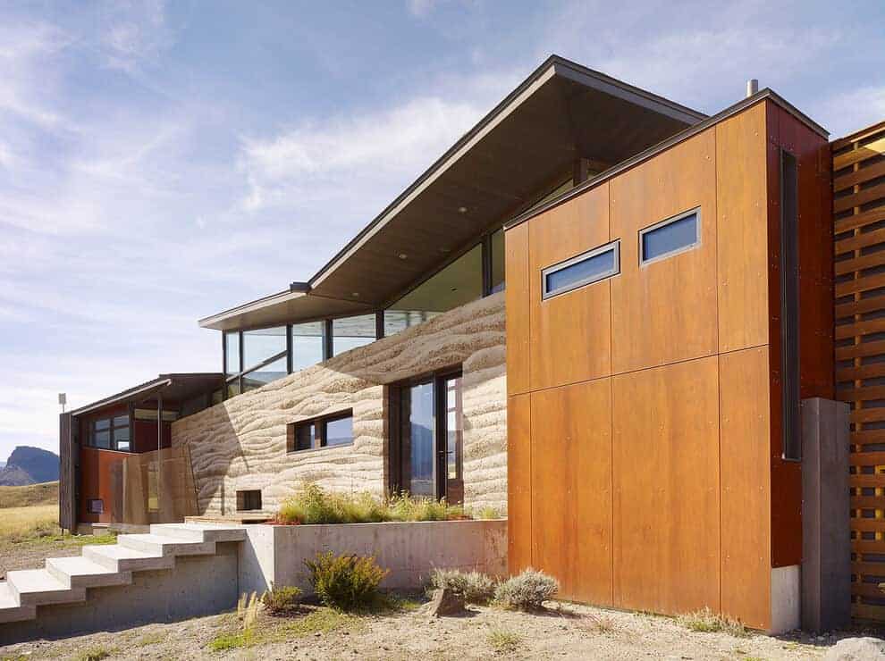Modern sustainable house with unique architectural design, combining concrete, wood, and glass elements, set in a scenic landscape.