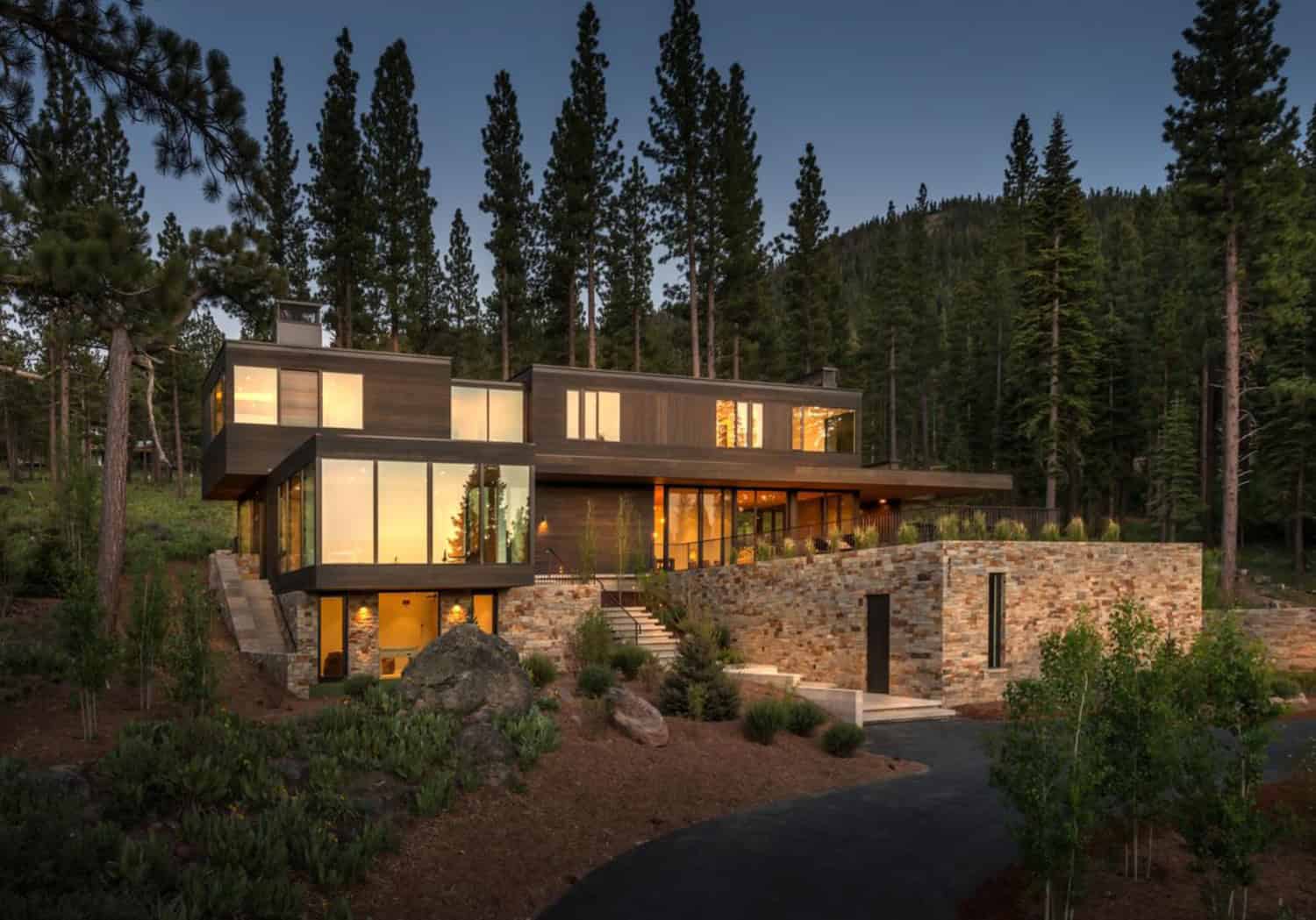 Modern mountain retreat with contemporary architecture, large glass windows, and natural stone accents nestled among tall pine trees.