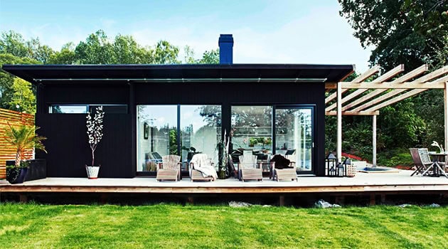 Modern black contemporary house with large glass sliding doors and an outdoor deck, surrounded by greenery.