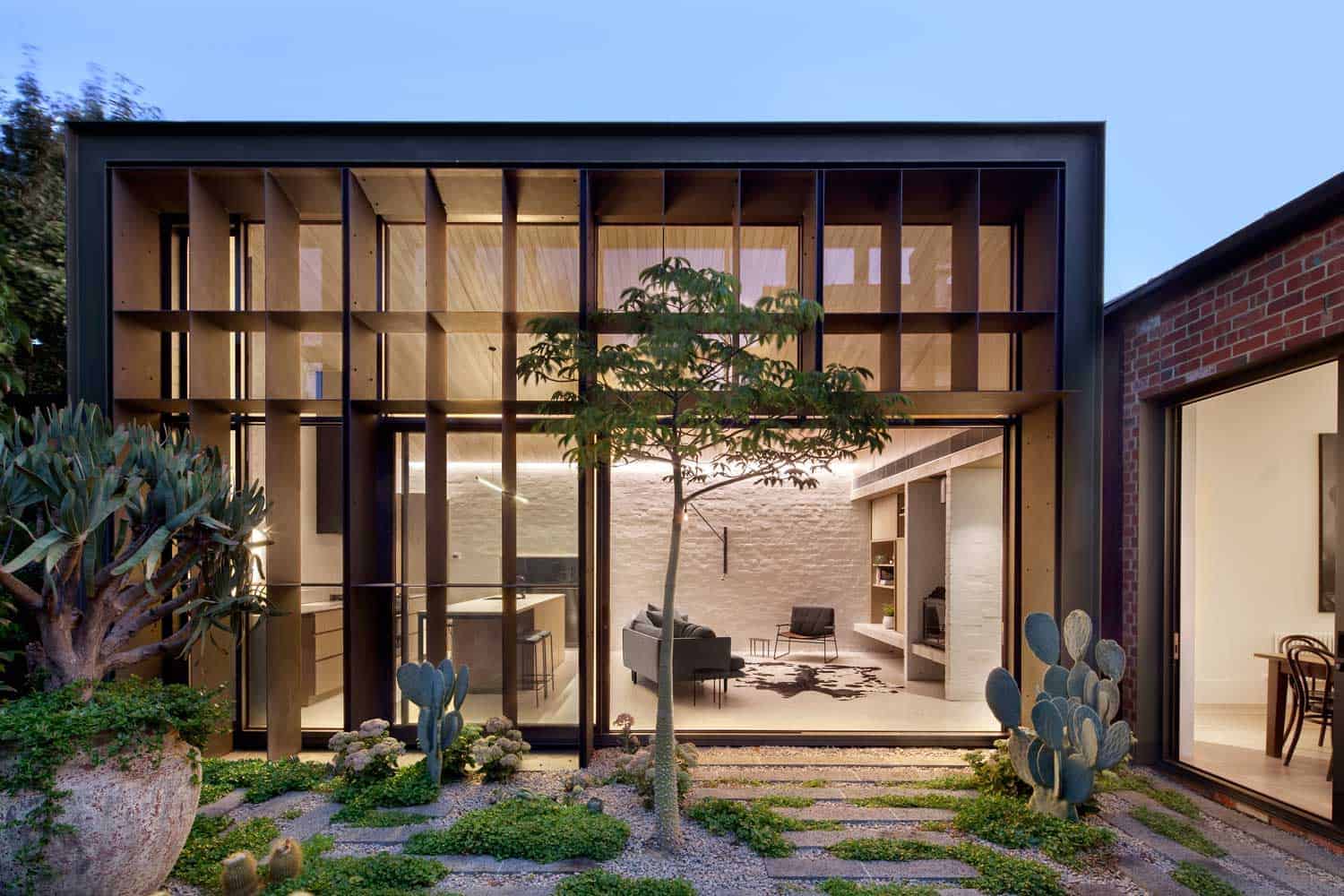 Modern glass façade of contemporary home with wooden accents, landscaped garden, and trees, showcasing innovative architecture and sleek interior design.