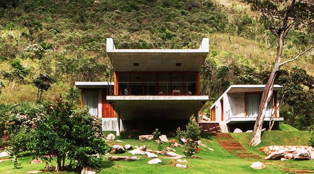 Modern hillside house with contemporary architectural design, large glass windows, and lush landscaped surroundings.
