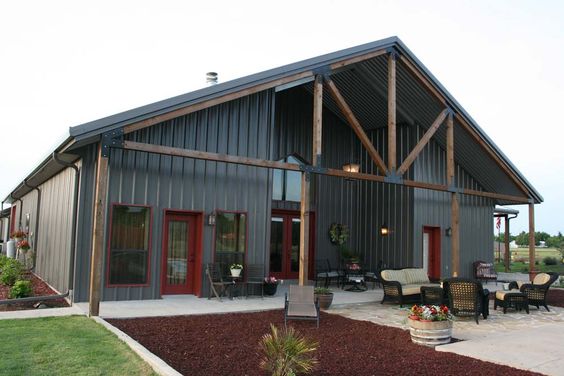 Modern black metal barn-style home with wood accents, large outdoor seating area, and contemporary exterior design, perfect for rustic-modern architecture enthusiasts.