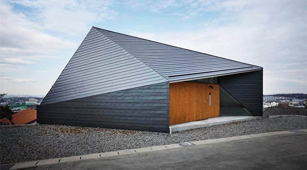 Sleek modern black house with angular architectural design and wooden door, situated on a gravel roof, exemplifying contemporary architecture and innovative residential design.