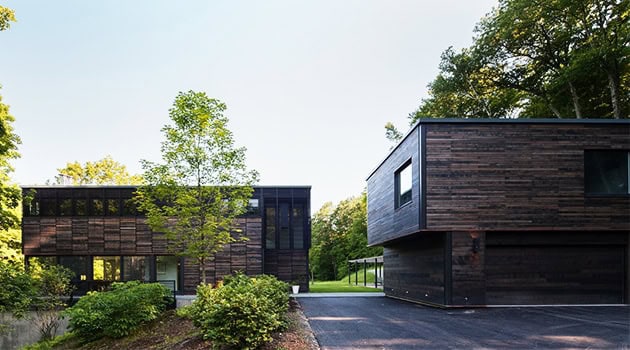 Contemporary modern house with dark wood exterior, surrounded by lush greenery, showcasing innovative architectural design and sustainable construction.