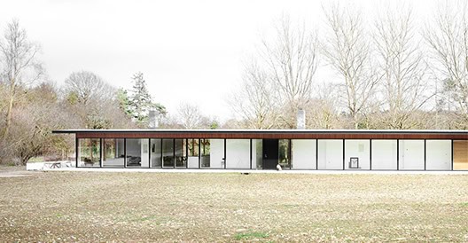 Modern single-story house with large glass windows and minimalist design surrounded by a natural landscape.