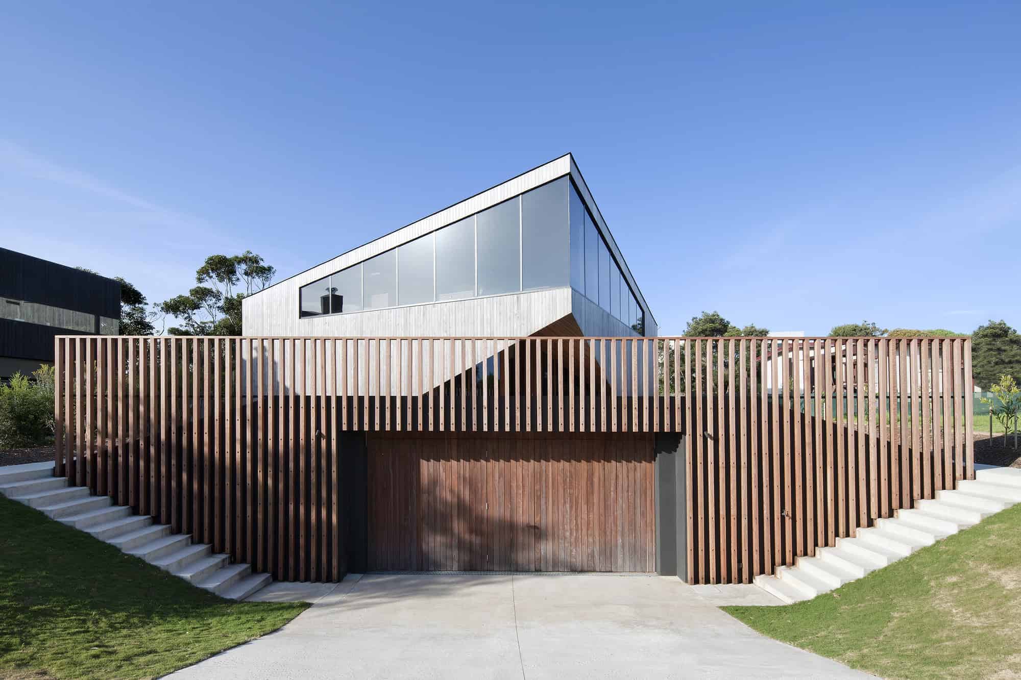 Sleek modern house with contemporary architecture featuring wood slat fencing and large glass windows, set in a scenic landscape with a blue sky.